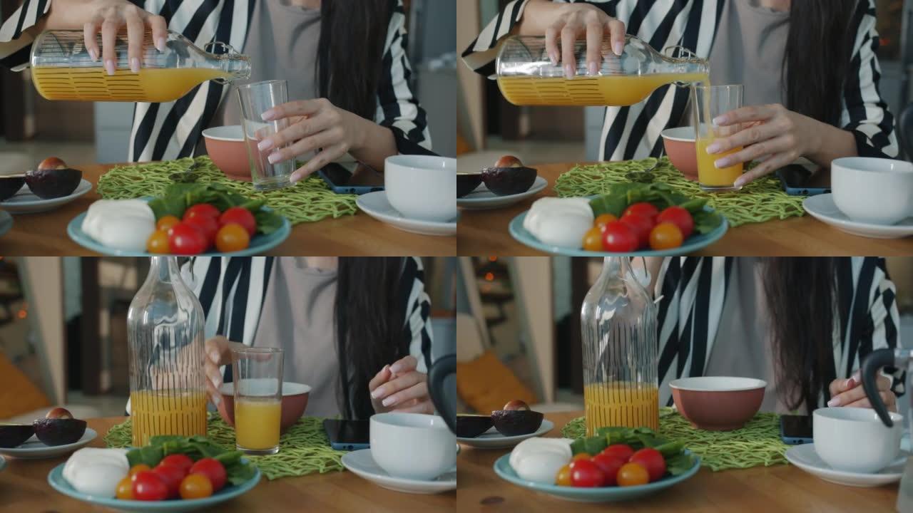 在家早餐时女性手在玻璃杯中倒果汁和饮用的特写