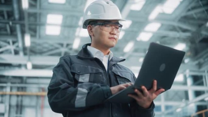 穿着安全制服和安全帽的专业重工业亚洲工程师/工人的肖像使用笔记本电脑。自信的中国工业专家站在工厂里。
