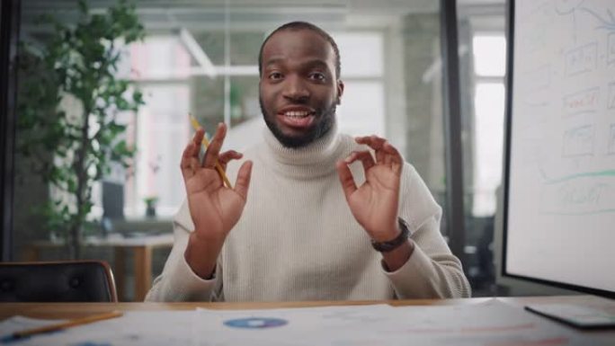 从镜头的角度来看，英俊的年轻黑人项目经理在创意办公环境中进行视频通话。快乐的非洲裔美国男性专家通过实