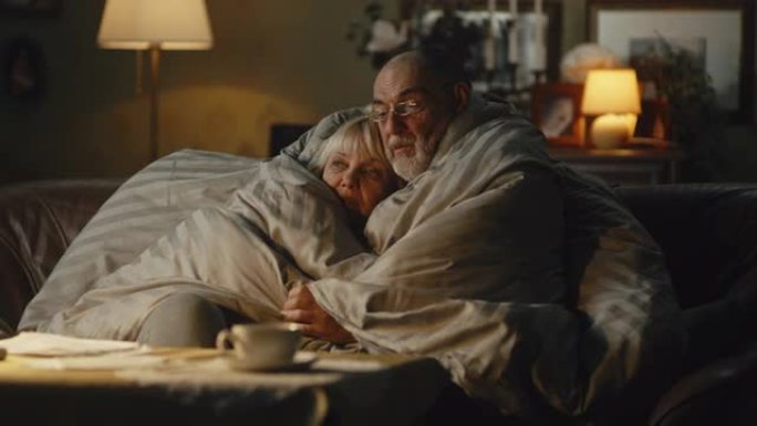 悲伤的老年夫妇拥抱在毯子下聊天