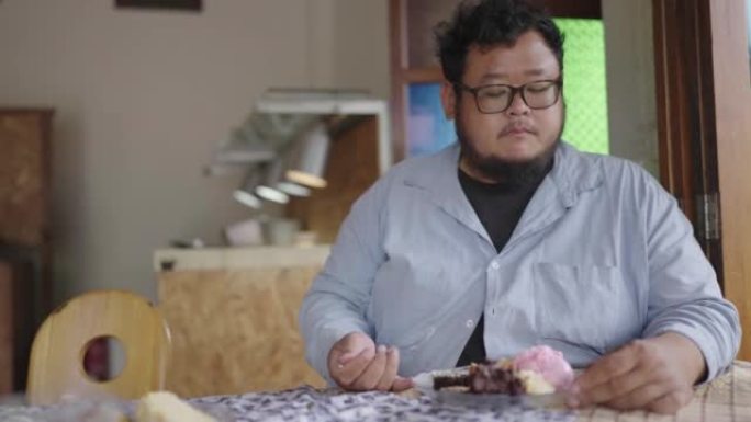 SLO MO: 一个胖子用手吃一块西瓜，用叉子在咖啡馆里满意地吃冰淇淋和甜点的前视图。