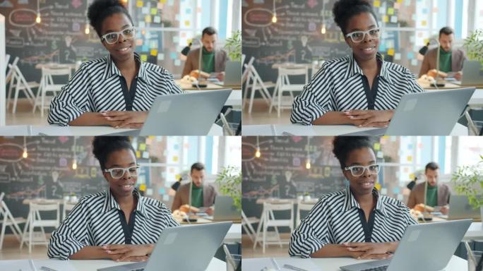 坐在共享办公室的办公桌前微笑的美国黑人商务女士的慢动作肖像