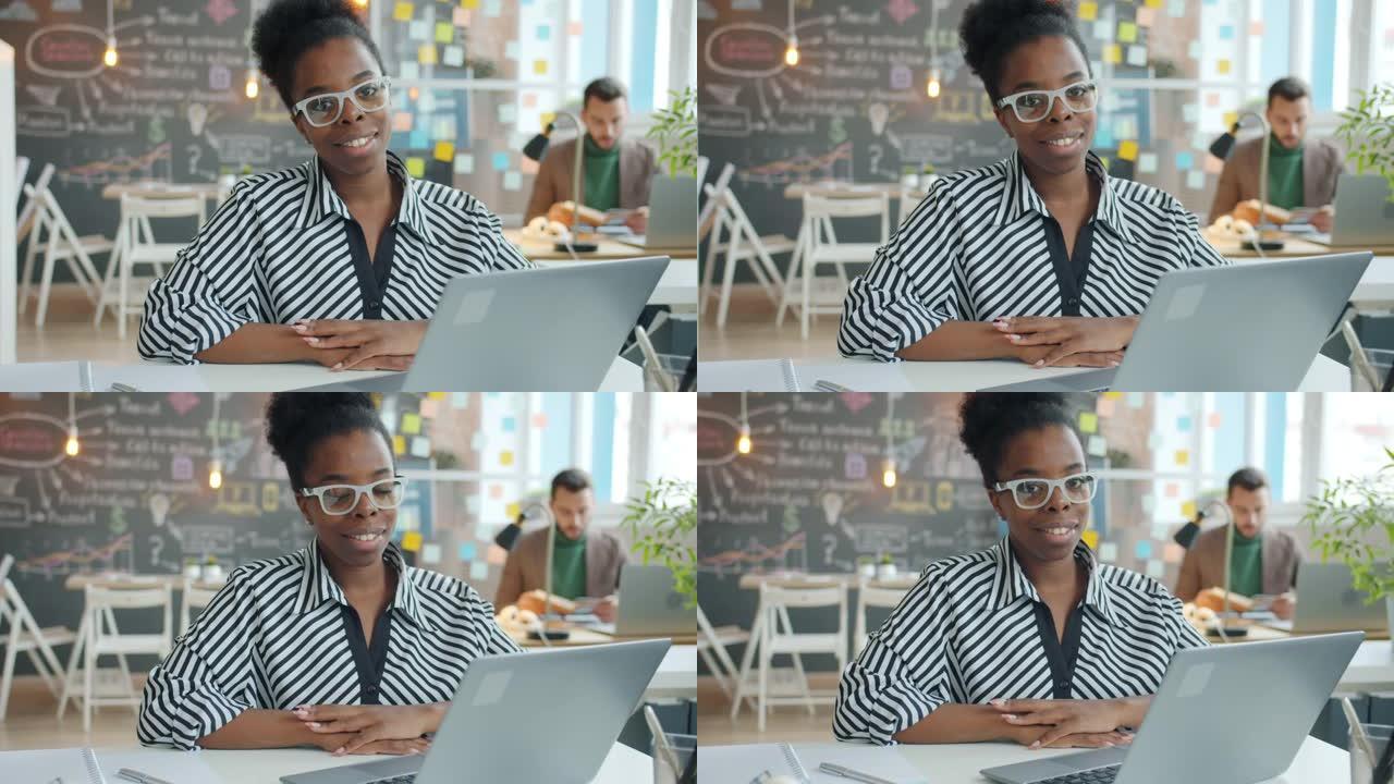 坐在共享办公室的办公桌前微笑的美国黑人商务女士的慢动作肖像