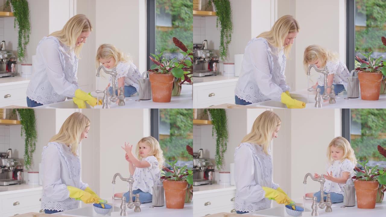 母亲在家，女儿在厨房的水槽里做家务，戴着橡胶手套洗衣服