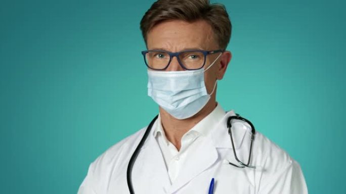穿着医用口罩的英俊男医生在室内慢动作的肖像。人和传染病。医务人员白色实验室外套和眼镜。医学概念。