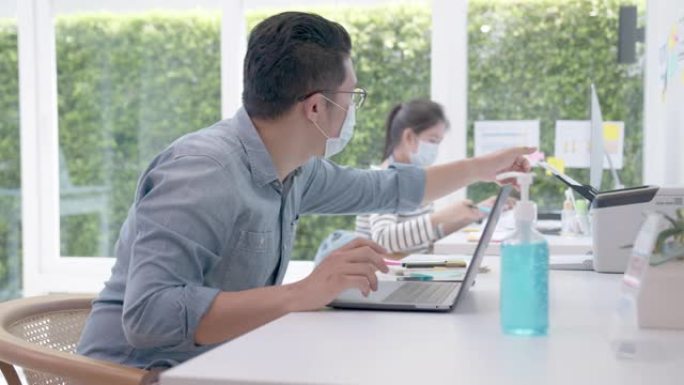 在办公室使用笔记本电脑开始工作之前，男人戴上口罩并用酒精凝胶清洁手部消毒。电晕病毒危机后的新常态、社
