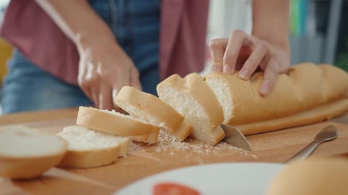 年轻的亚洲女厨师的手拿着刀在家里厨房桌子上的木板上切全麦面包。