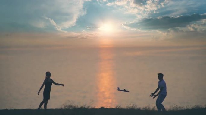 男孩和女孩把玩具飞机扔在日落背景上