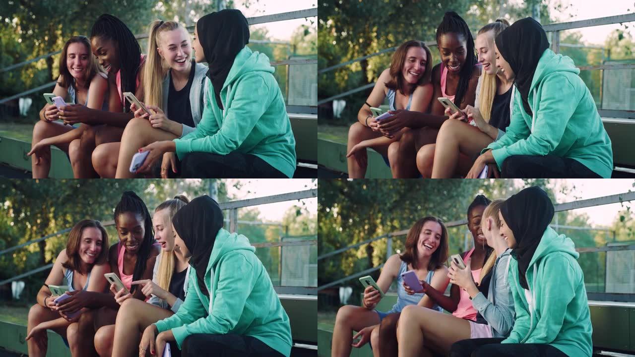 一群年轻的多种族女性青少年坐在公园里，在智能手机上观看有趣的视频。一群朋友在户外一起玩乐，同时保持联