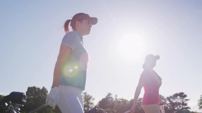 两名白人女性高尔夫球员带着他们的高尔夫球具推车在高尔夫球场上行走