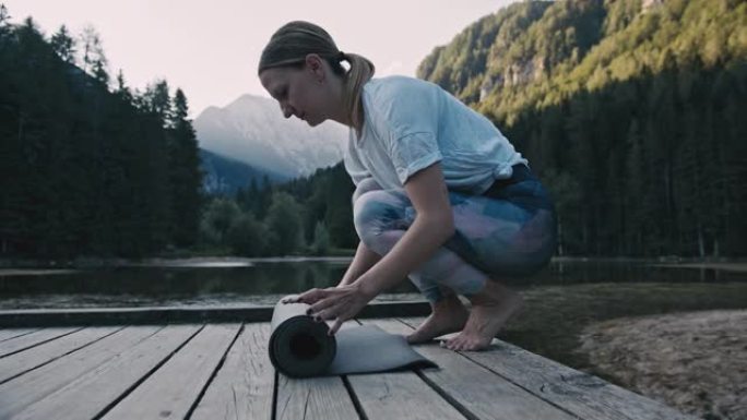 金发碧眼的成年女子穿着运动服躺在杰泽斯科湖前的木板路上的瑜伽马特