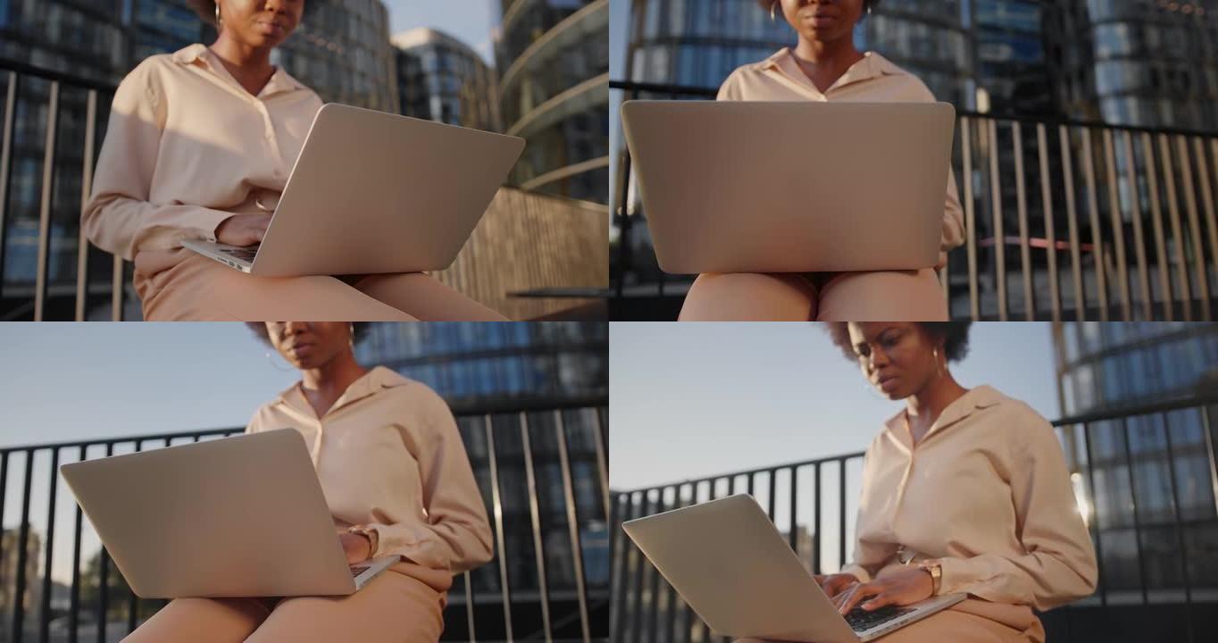 一个皮肤黝黑的年轻卷发女商人在美丽的傍晚阳光下对着商务中心在笔记本电脑上输入一条消息