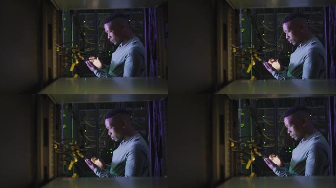使用智能手机在商务服务器机房工作的非洲裔美国男性计算机技术人员