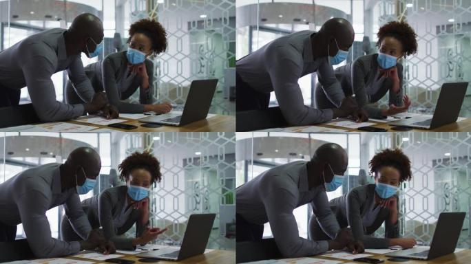 戴着口罩讨论，在办公室使用笔记本电脑的男女商业同事