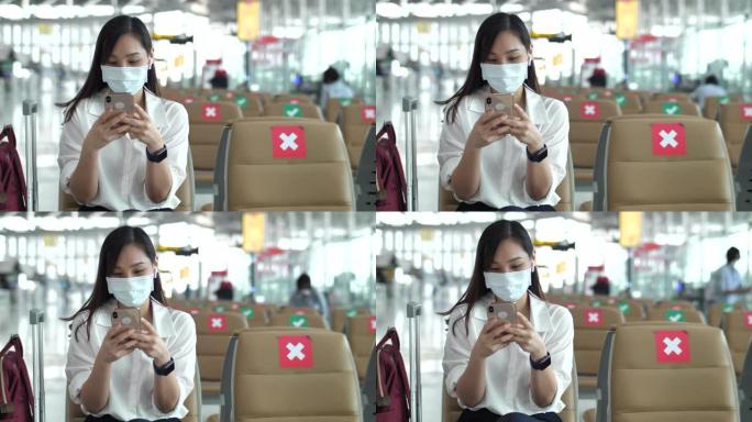 年轻的亚洲妇女在机场使用智能手机戴防护口罩坐在新空间社交距离