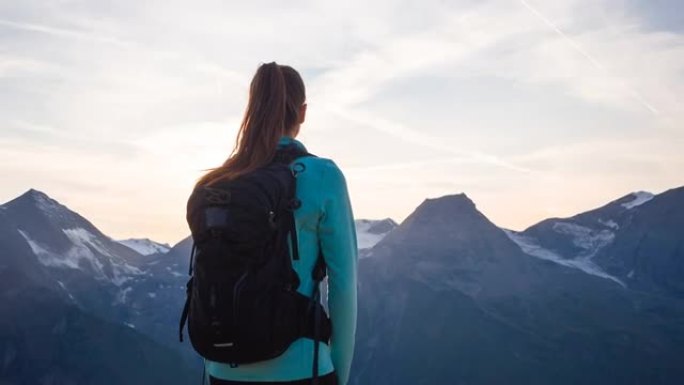 女徒步旅行者站在山顶上，在日落时欣赏山谷的壮丽景色