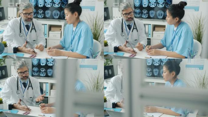 在现代诊所中，穿着磨砂膏的护士看着平板电脑屏幕并与白大褂的医生交谈