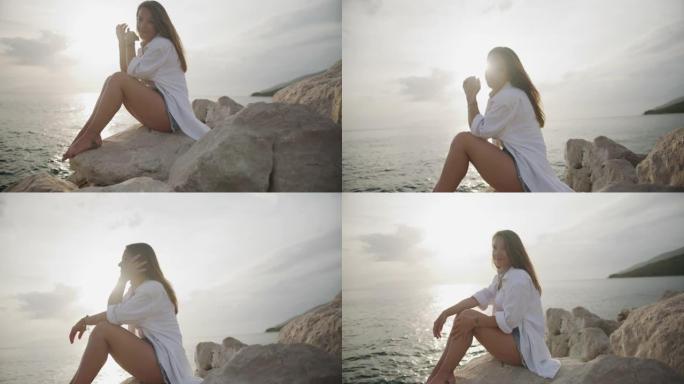 快乐的年轻女子坐在海滩上的岩石上的肖像
