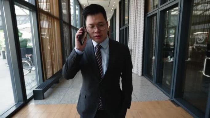 亚洲商人在穿过酒店走廊时用手机交谈