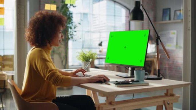 一位在创意机构工作的多民族专家的肖像。时尚富有表现力的黄色套头衫女性使用带绿屏模拟显示的台式电脑。