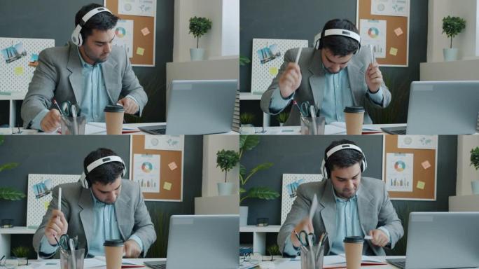 快乐的商人戴着耳机在办公室的办公桌上享受音乐