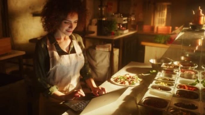 在餐厅: 美丽的女厨师使用笔记本电脑。正宗的比萨店，配有美味的有机生态食品。在她的小型企业家庭商店工