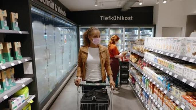 戴着口罩的成年妇女在超市购买杂货