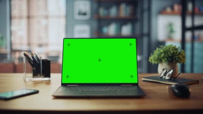 笔记本电脑，带有模拟绿屏显示屏，站在舒适的客厅的桌子上。在背景中，时尚的现代明亮的家庭办公室工作室白