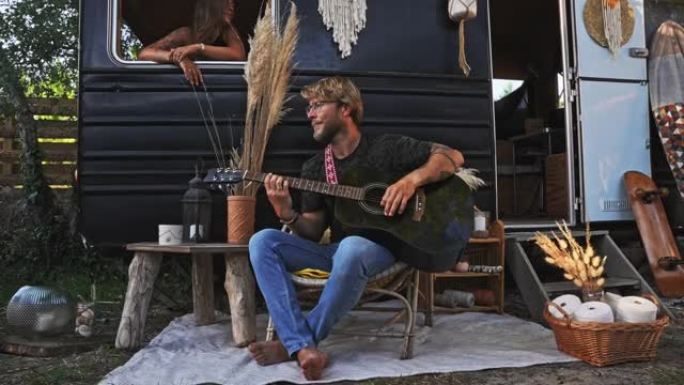 WS年轻的嬉皮士男子弹吉他，而女友则喜欢露营者内部的音乐