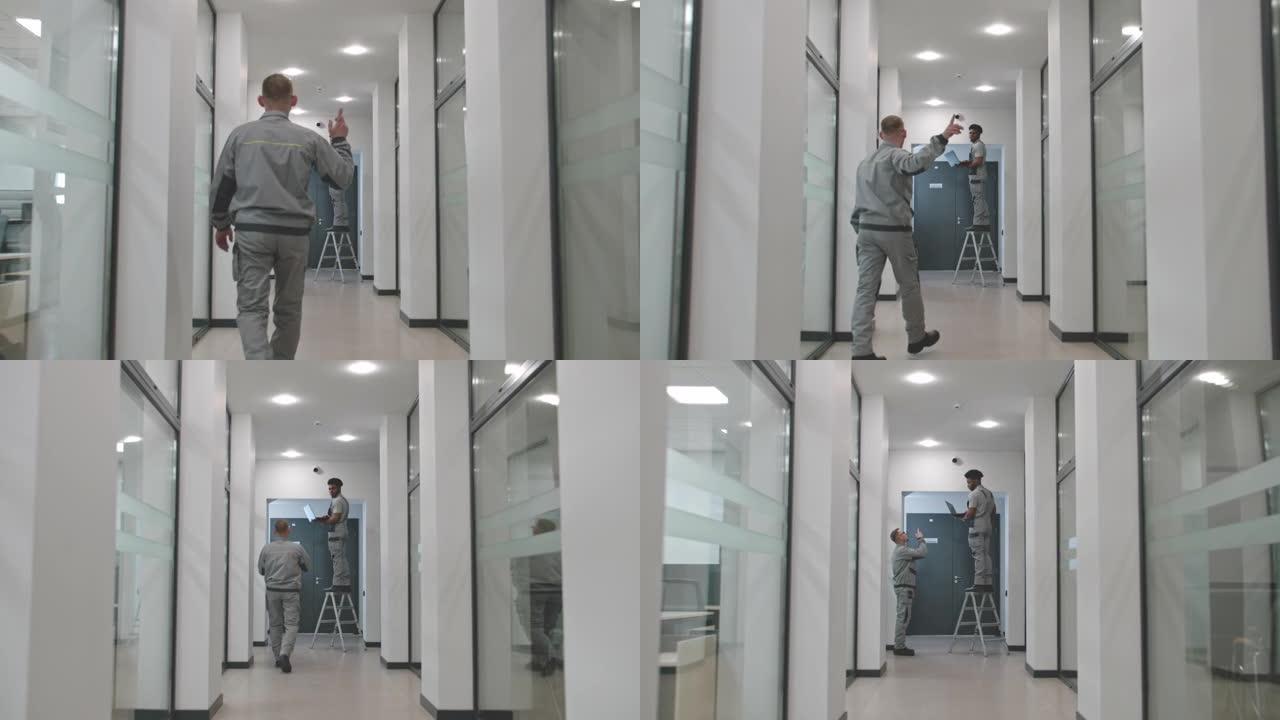 两名穿着制服的安装人员使用笔记本电脑在走廊上设置安全摄像头