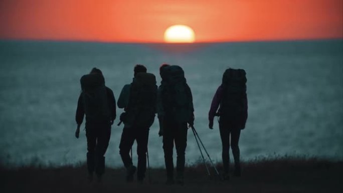 四位旅行者在日落背景下步行到海边。慢动作