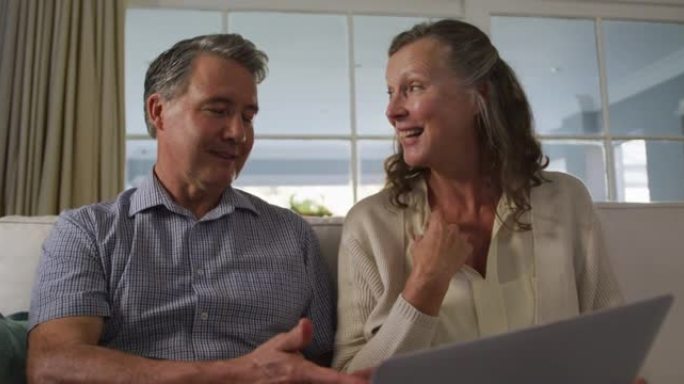 快乐的白人高级夫妇坐在客厅里用笔记本电脑聊天