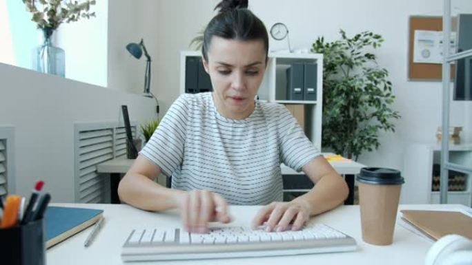 劳累过度的年轻女子用电脑键盘打字，用疯狂的脸匆匆看着相机