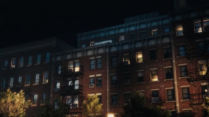 VFX动画砖多层公寓楼的低角度平移镜头。旧翻新的褐砂石房子。带有紧急楼梯和路灯的房屋夜间的城市景观。