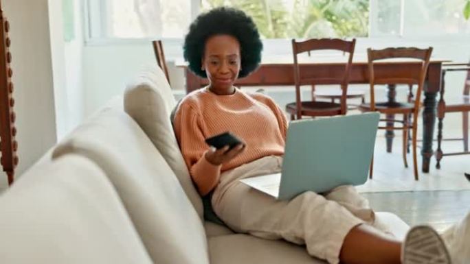 非洲妇女在客厅沙发上的笔记本电脑上工作，注意到智能手机并嘲笑电话文本。借助数字创新，5g在线互联网和