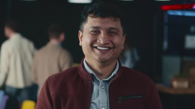 快乐的年轻兴奋的40多岁印度团队领导商人，公司老板在模糊的办公室背景下对着镜头微笑。