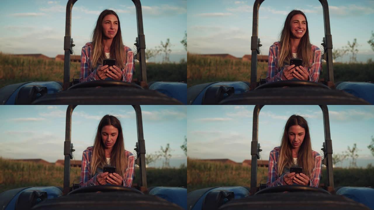 日落时坐在拖拉机上，微笑着笑着使用智能手机的女人的肖像。女性农民保持联系并使用互联网改善业务