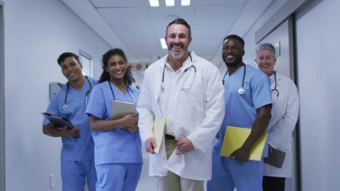 医院走廊上穿着磨砂膏和实验服的微笑男女医生的多元化群体