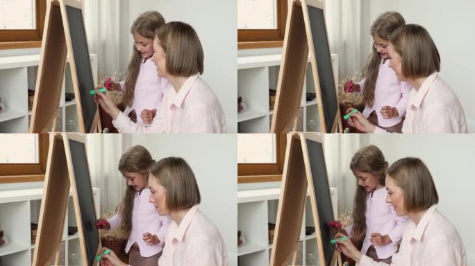 快乐妈妈和小女儿女孩在小黑板上画画