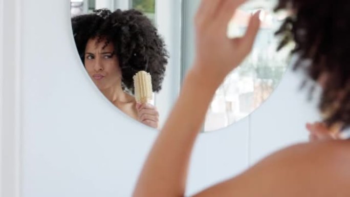 浴室，与一名黑人妇女在家里准备时在镜子里梳头跳舞。有趣、快乐和顽皮的年轻女性在思考护发时开玩笑