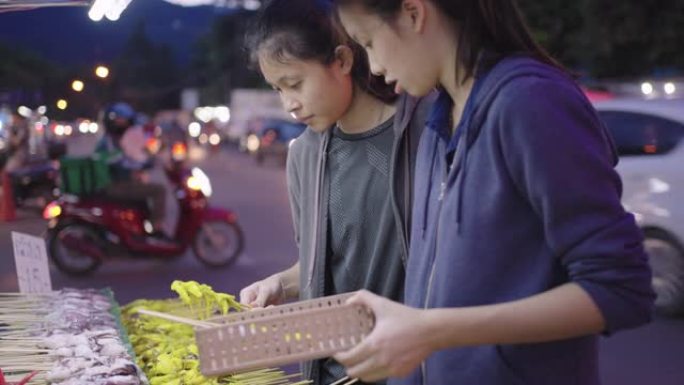 年轻的亚洲女孩选择生鱿鱼在夜市烧烤。泰国街头小吃。