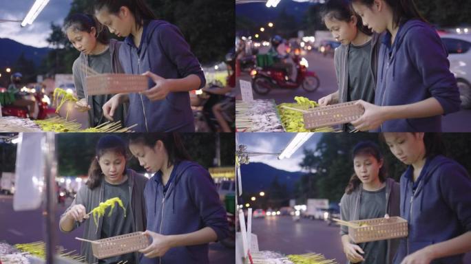 年轻的亚洲女孩选择生鱿鱼在夜市烧烤。泰国街头小吃。
