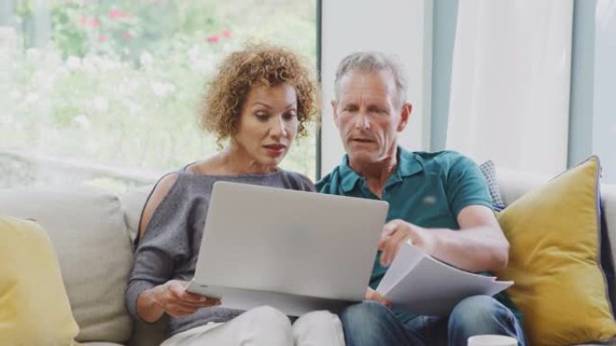 高级退休夫妇坐在家里的沙发上，用笔记本电脑查看个人财务状况