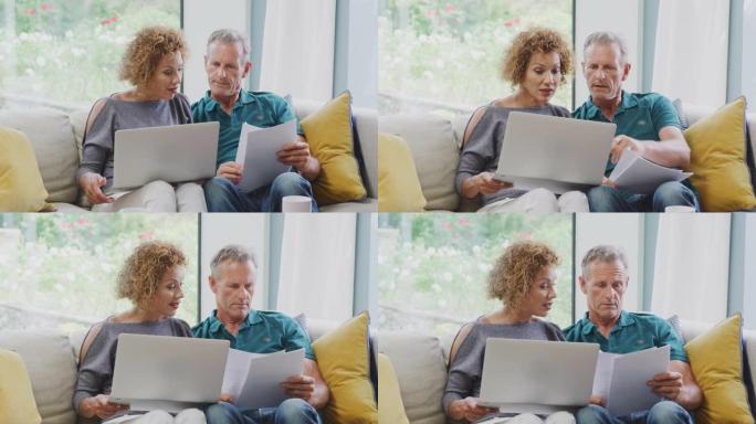 高级退休夫妇坐在家里的沙发上，用笔记本电脑查看个人财务状况