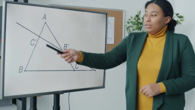 非裔美国妇女的肖像在遥远的课堂上教授几何，指向电子板并解释