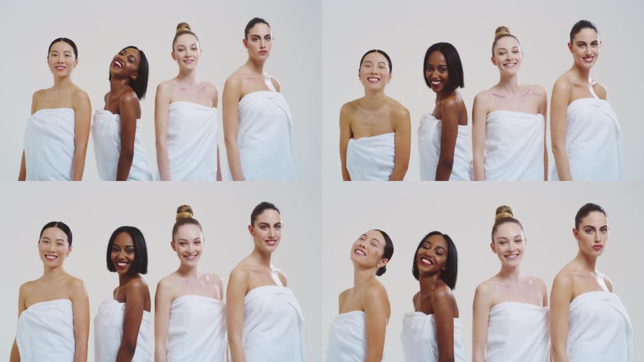 慢动作美丽的年轻微笑的女人不同的种族与完美的坚定和苗条的身体在白色浴巾跳舞和有趣的隔离在白色的背景。