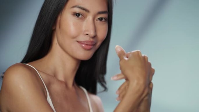女性美女肖像。美丽多样的亚洲黑发女人摆姿势，微笑着，用自然健康的皮肤触摸她的手。柔软孤立背景下的健康