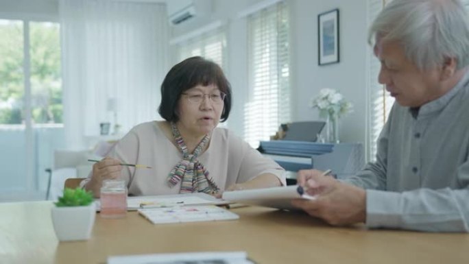 迷人的年轻亚洲公民夫妇坐在家里水彩画艺术品桌子上，在精神卫生治疗或亚洲老年人检疫活动生活方式概念中感