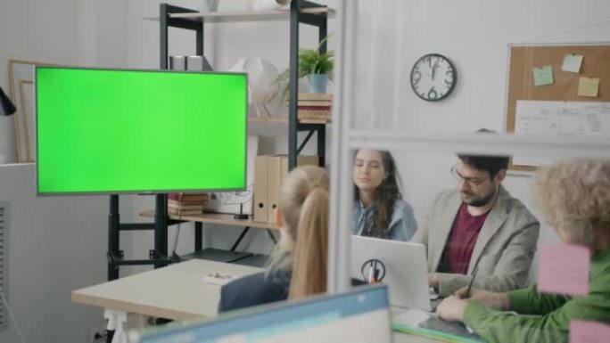 一群员工在办公室商务会议期间看着绿色色度键屏幕并交谈