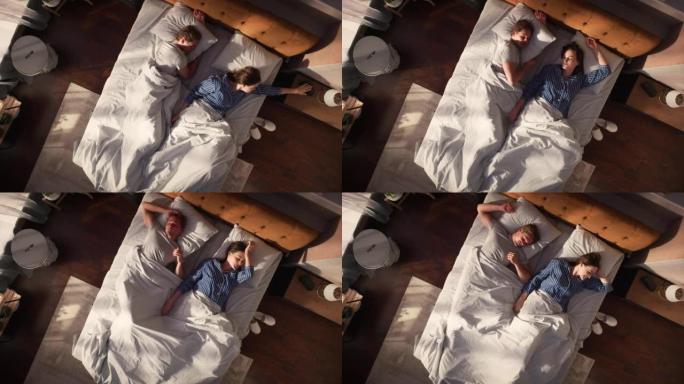 顶景公寓: 美丽的年轻夫妇睡在床上，阳光照在他们身上，他们互相看着对方，迎接新的晴天。两口之家的快乐
